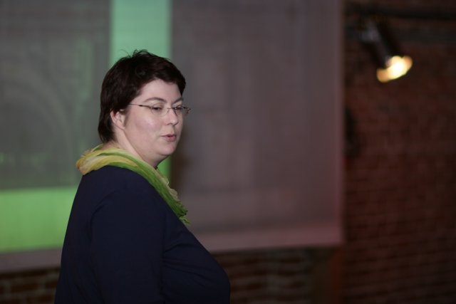 Woman with glasses and green scarf presenting in front of projector screen
