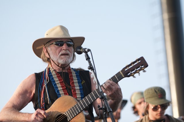 Willie Nelson Rocks the Okeechobee Music and Arts Festival Caption: Country legend Willie Nelson takes the stage in his signature cowboy hat and sunglasses, strumming his guitar and singing for the ecstatic crowd at the 2007 Okeechobee Music and Arts Festival.
