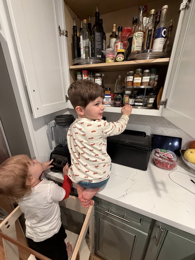Brothers Reaching for Spices in Kitchen Cabinet