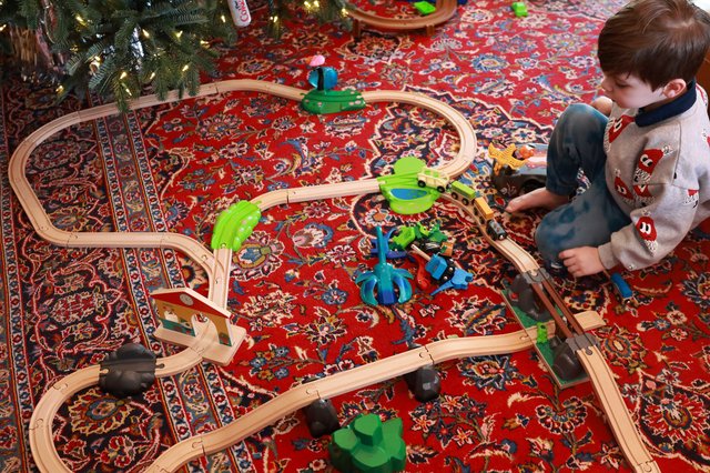 Child Playing with Wooden Train Set Under Christmas Tree