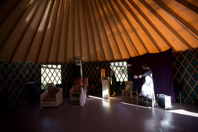 Center Stage in the Yurt Caption: A solo performer commands attention in the cozy yurt setting, surrounded by warm lighting and rustic furniture.
