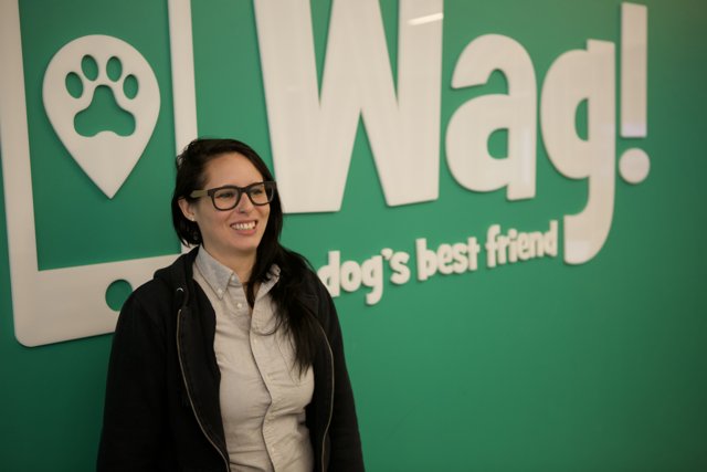 Smiling Woman Stands Proudly in Front of Wag Sign