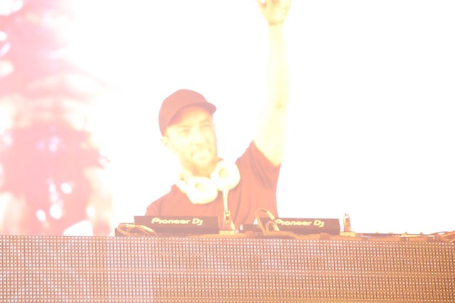 DJ Raises Hand Amid Blazing Stage Lights at Festival