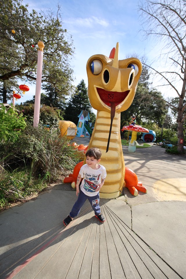 Young Boy Walking Past Giant Dragon Slide at Theme Park