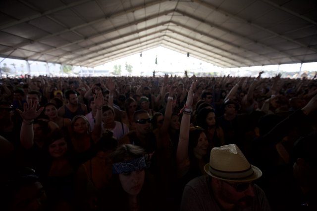 Hands Up for the Music Caption: A crowd of ten people with fedoras and cowboy hats raise their hands in excitement at Coachella 2012.