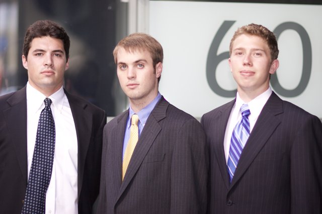 Three Men in Suits Pose in Front of a Sign