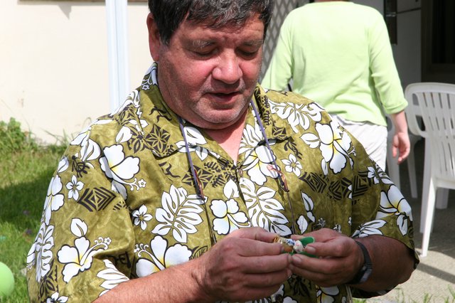Man in Hawaiian Shirt Examining Small Object Outdoors