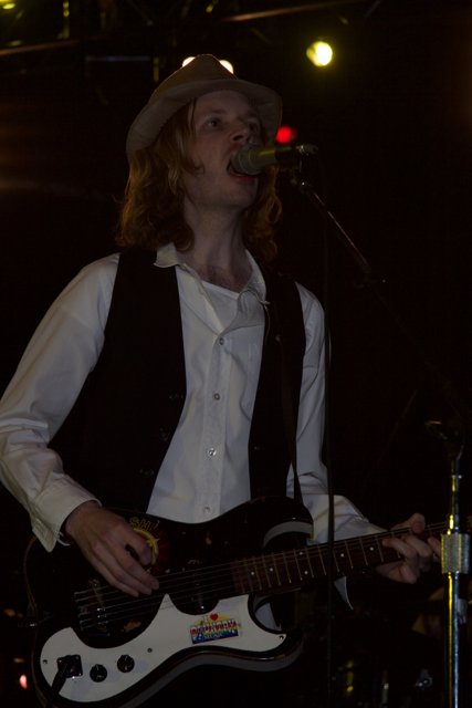 Beck's Musical Detour Caption: Beck mesmerizes the crowd with his guitar playing and soulful singing during his 2006 Detour album tour, wearing his signature fedora hat and bathed in a warm spotlight.