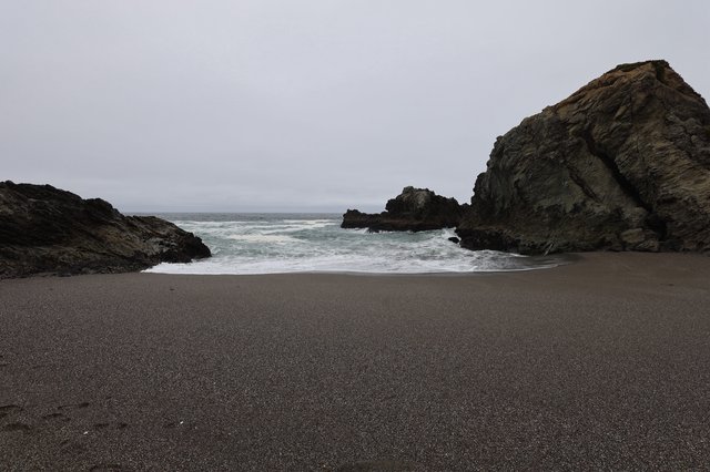 Secluded Cove with Dark Sand and Crashing Waves