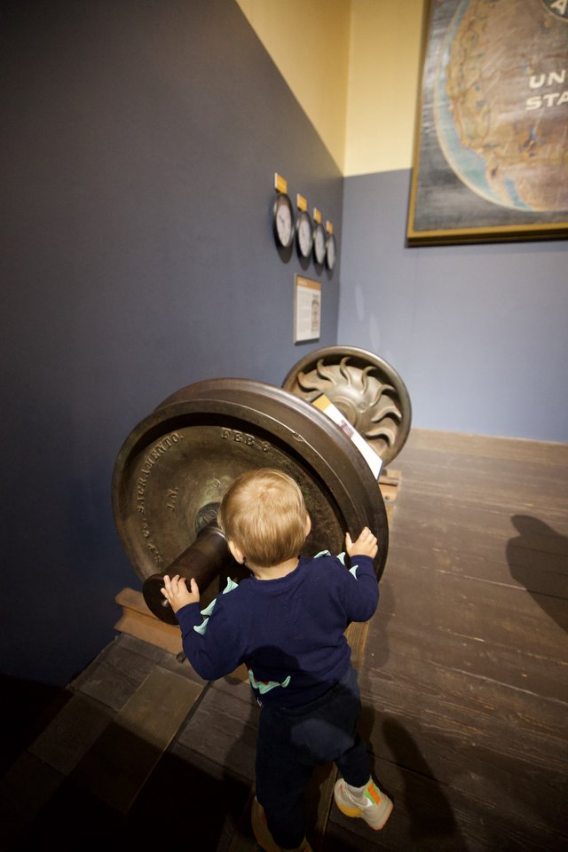 Young Child Exploring Antique Train Wheel at Museum