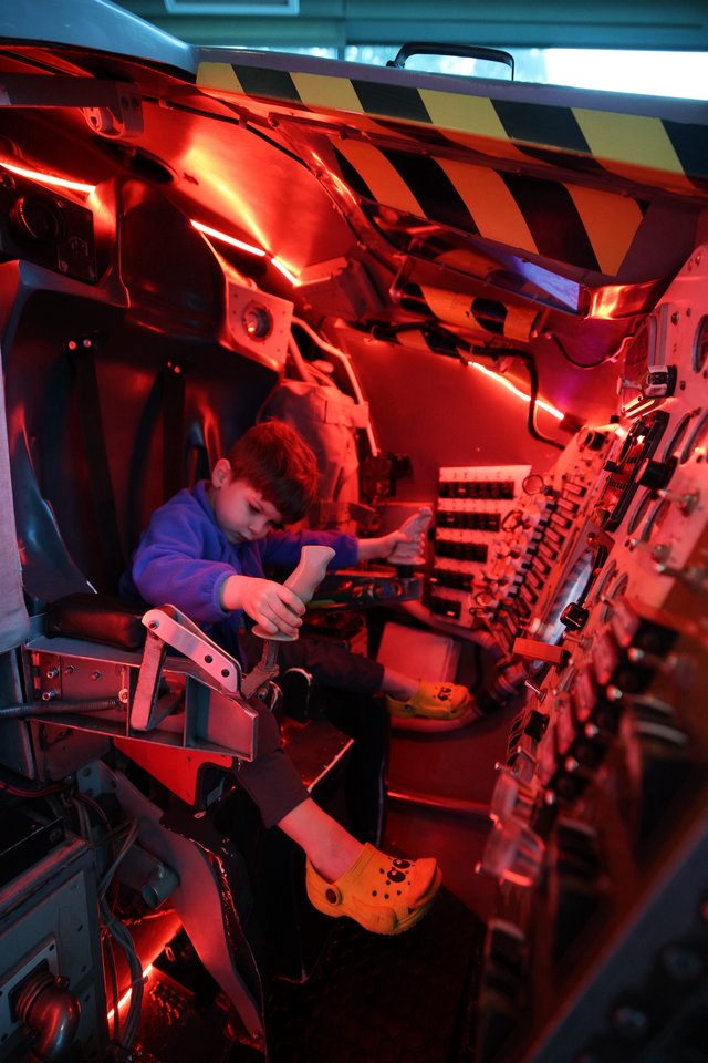 Young Visitor Explores Spacecraft Interior Under Red Emergency Lighting