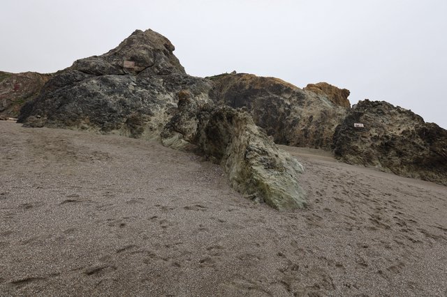 Ancient Coastal Rocks Emerging from Gray Sandy Beach