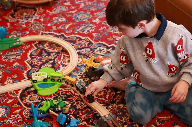 Child Playing with Wooden Train Set on Persian Rug