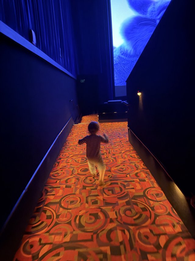 Child Running Through Illuminated Carpet Hallway in Dark Museum