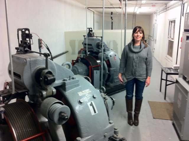 Woman Poses Beside Historic Elevator Machine Room Equipment