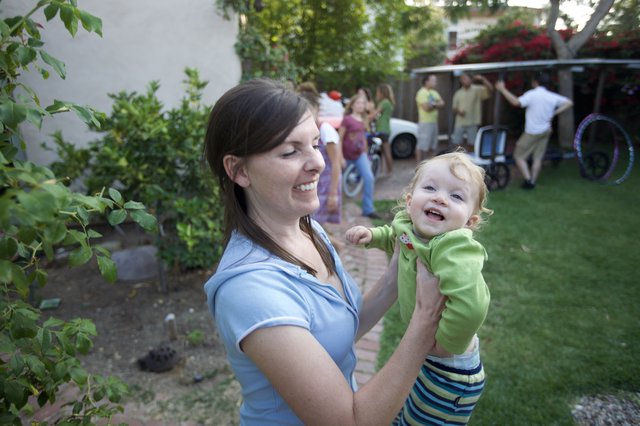 Joyful Mother Lifting Laughing Baby at Backyard Party