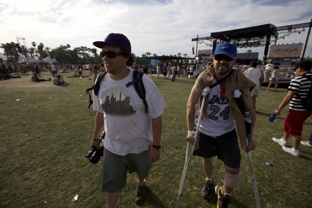Overcoming Obstacles Caption: Two men in baseball hats walk on crutches through the lively Coachella crowd.