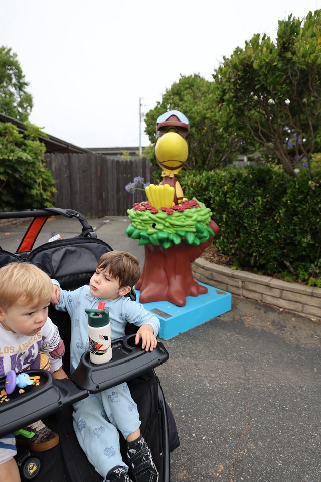 Two Young Boys in Stroller Near Cartoon Bird Statue