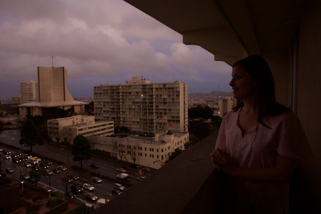 Woman Gazes Over City at Twilight from Balcony
