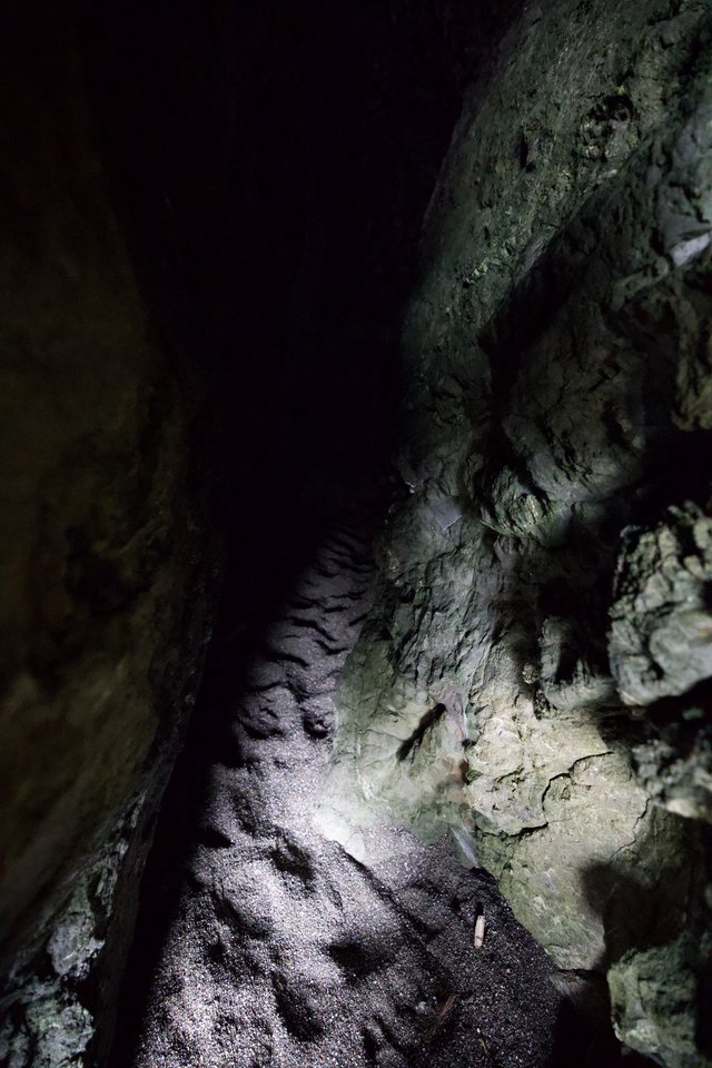 Darkness Ahead: Narrow Cave Passage Illuminated by Flashlight