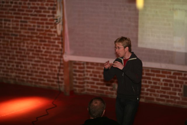 Man Speaking with Microphone in Hand in front of Brick Wall