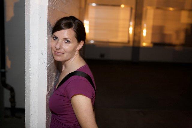 Woman Leans Against Wall With Playful Smile