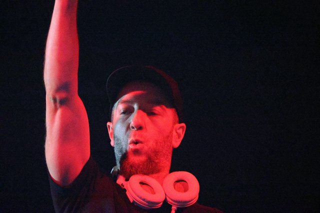 DJ Raises Hand Under Red Stage Lights at Wobbleland