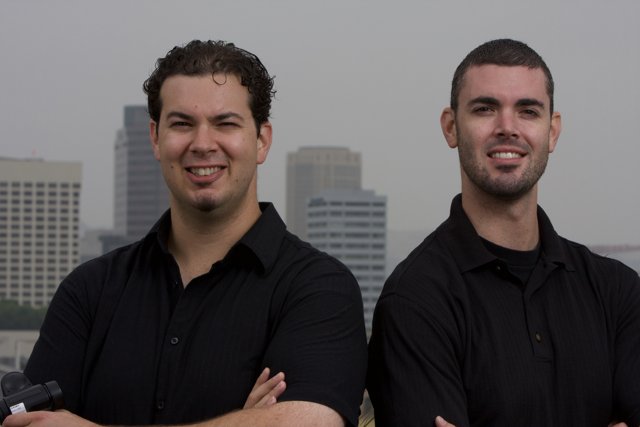 Two men in black shirts posing in front of a skyscraper