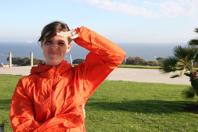 Woman in Orange Jacket Shielding Eyes by Coast