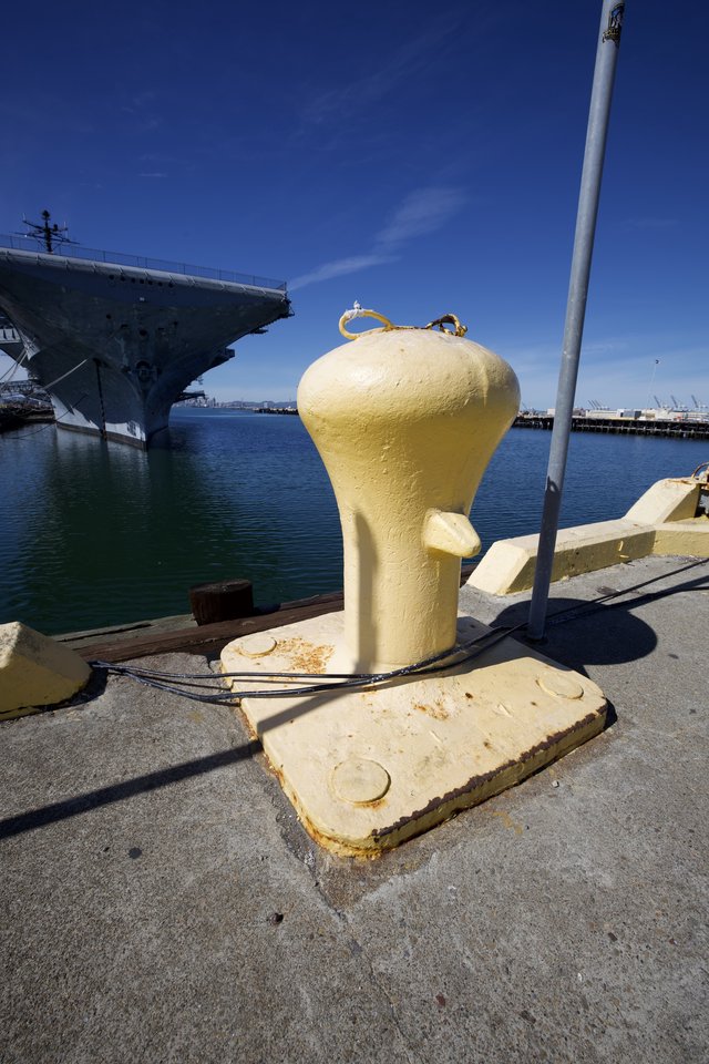 Yellow Mooring Bollard at Naval Harbor with Aircraft Carrier