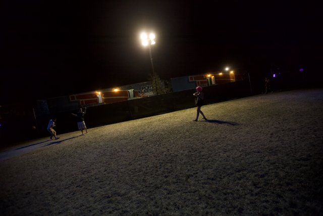 Nighttime Soccer Match Caption: A group of four people play soccer under the night sky, illuminated by the bright lights on a nearby lamp post.