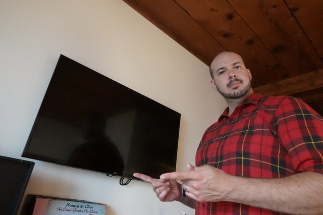 Man in Plaid Shirt Gesturing Toward TV