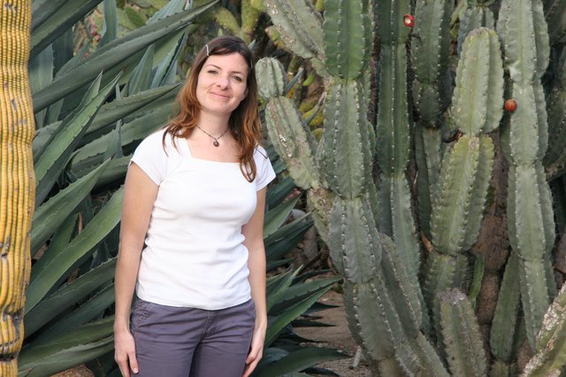 Woman Smiling Among Giant Cacti in Desert Garden