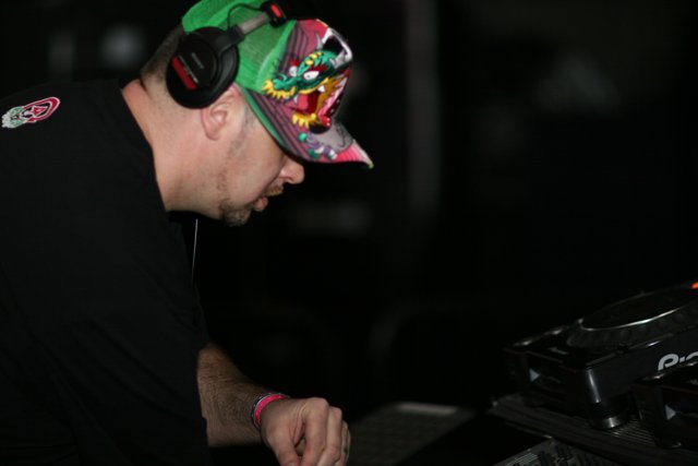 DJ in Action Caption: A male entertainer wearing a baseball cap, headphones, and a fingerless glove, while working with his turntable during a musical performance in 2006.
