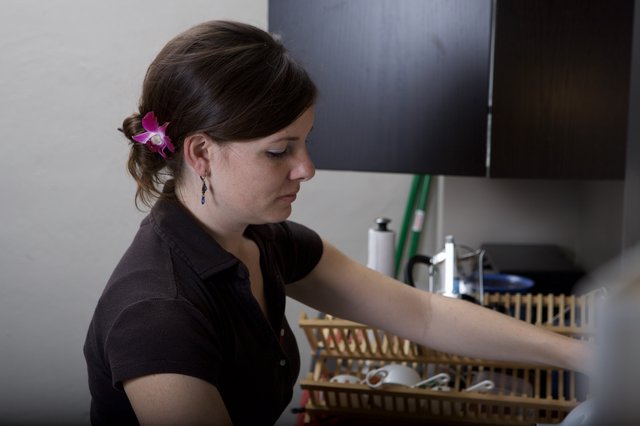 Woman with Orchid Arranges Dishes in Kitchen