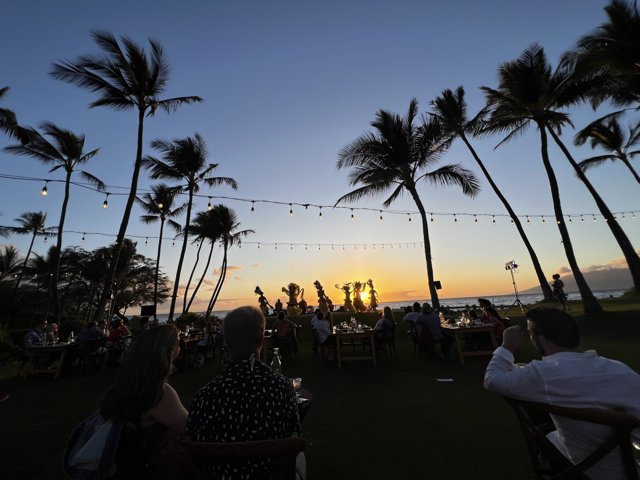 Sunset Dining Amongst the Palms Caption: 23 people enjoy a tropical evening at a restaurant in Wailea, Hawaii, surrounded by palm trees and the stunning colors of a Maui sunset.