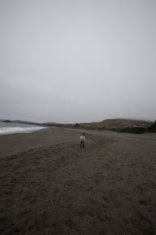 Small Child Standing Alone on Vast Foggy Beach