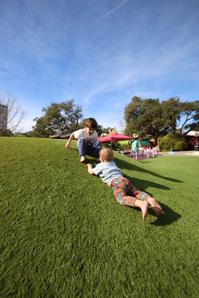 Brothers Playing Superman on Grassy Hill at Park