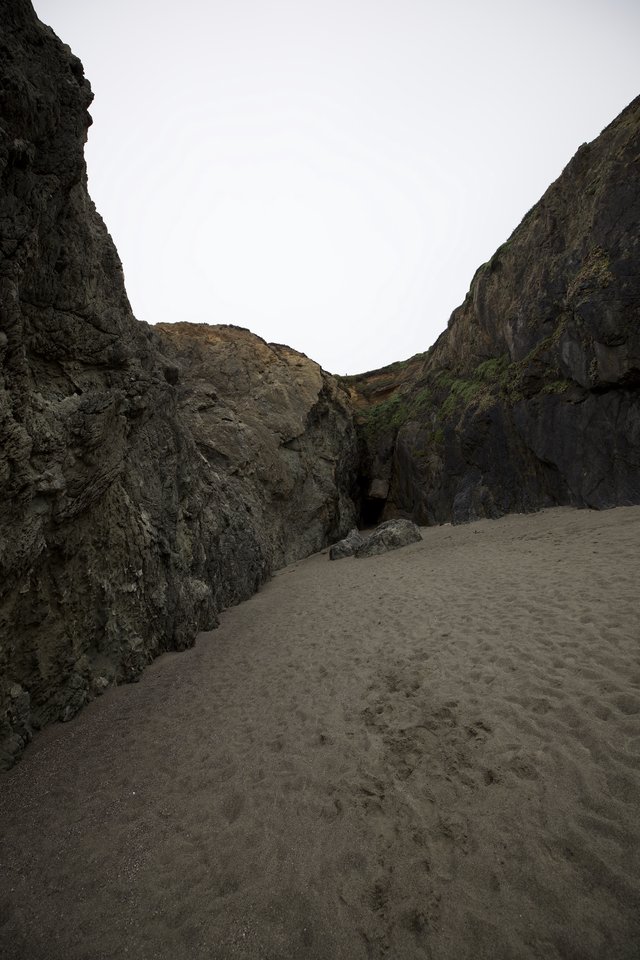 Dark Cave Opening Between Towering Coastal Sea Cliffs