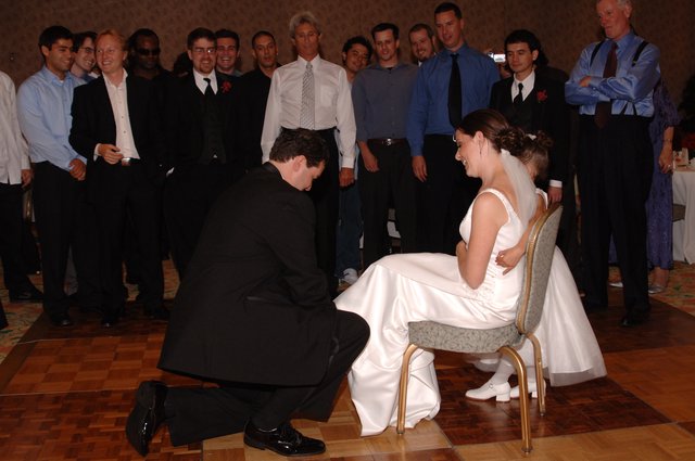 Groom Retrieves Garter from Laughing Bride at Reception
