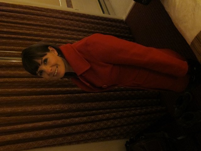Woman in Red Coat Smiling Over Shoulder Indoors