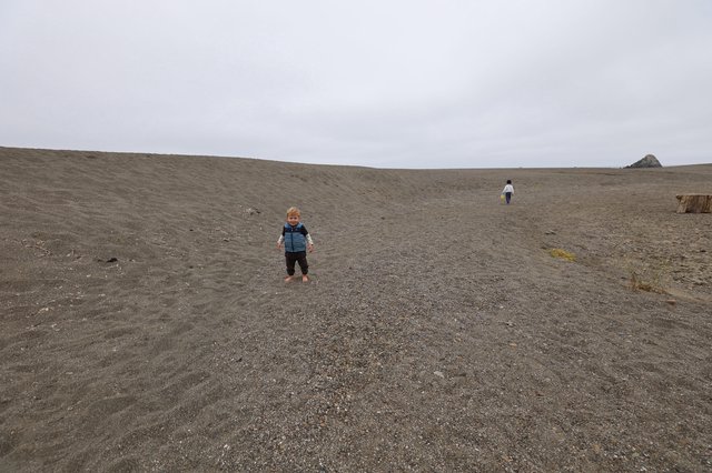Young Child Smiles on Vast Dark Sand Beach