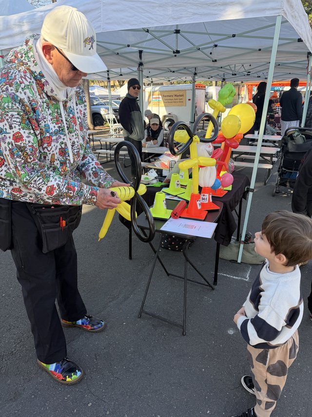 Balloon Artist Delights Young Child at Farmers Market
