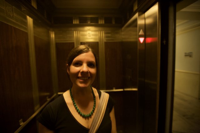 Smiling Woman in Warmly Lit Vintage Elevator