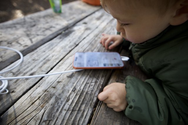Curious Toddler Explores Smartphone at Picnic Table