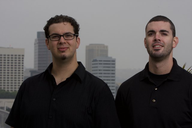 Two Happy Men in Black Shirts in Front of Skyscraper