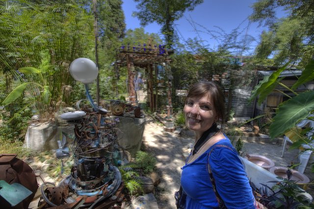 Woman Smiling Among Eclectic Junk Art Garden Sculptures
