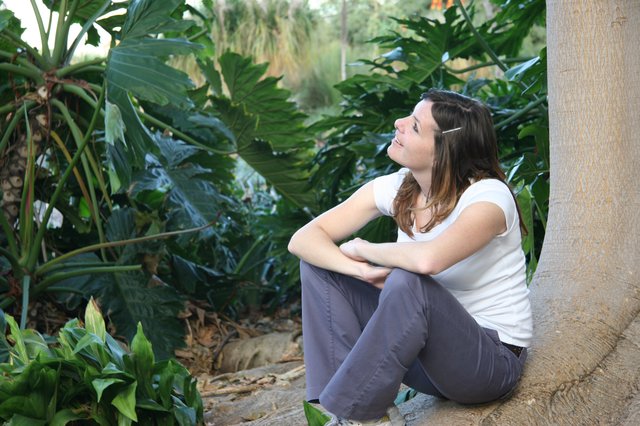 Young Woman Resting Against Palm Tree in Tropical Garden