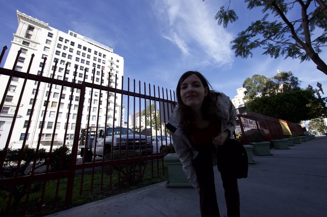 Woman Peering Through Iron Fence on City Sidewalk