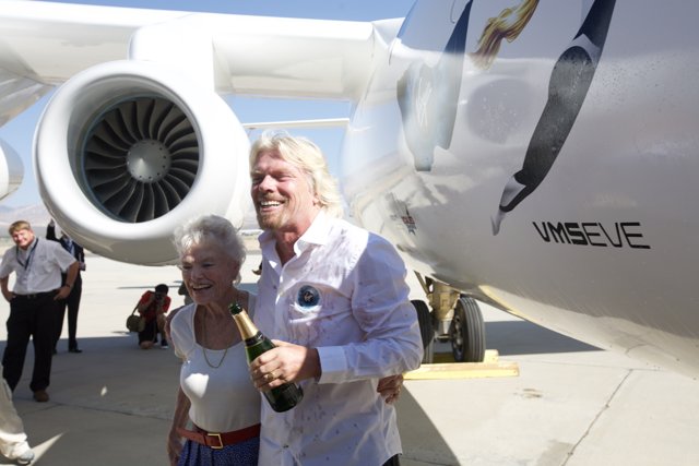 Richard Branson and a Companion Stand Tall Next to an Airplane
